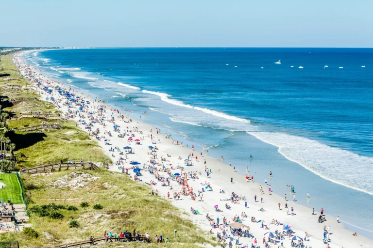 Beachgoers along a broad sandy shoreline beside blue ocean water.